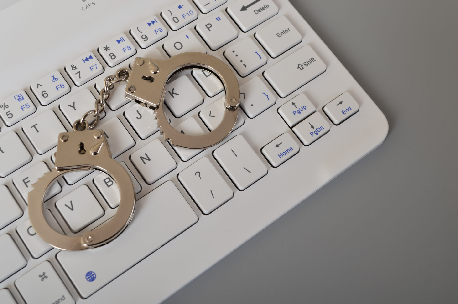 laptop keyboard and handcuffs isolated on a grey b 2023 01 03 16 29 10 utc
