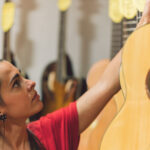 young woman picking up a guitar hanging in a shop 2022 05 03 23 08 20 utc