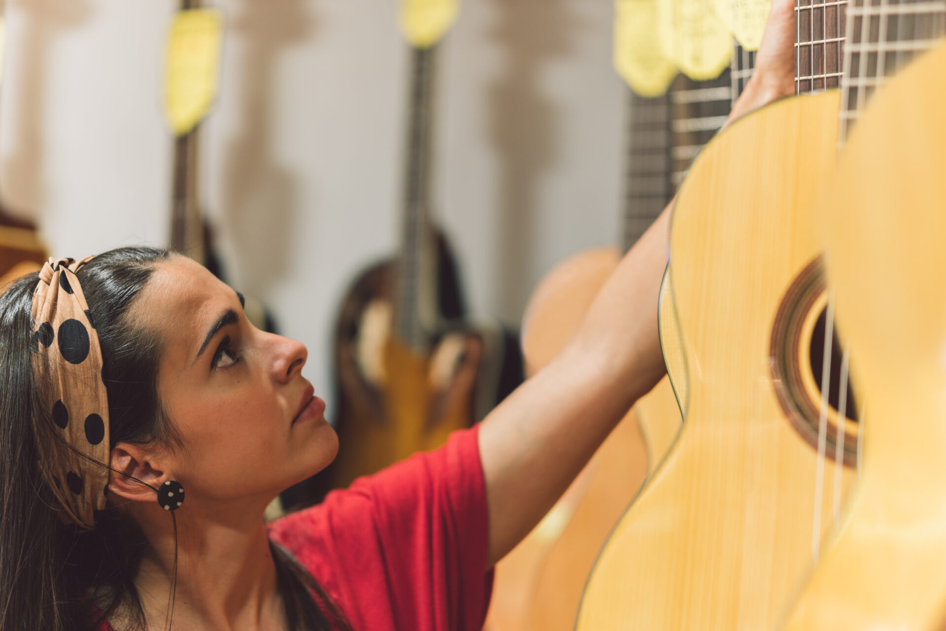young woman picking up a guitar hanging in a shop 2022 05 03 23 08 20 utc