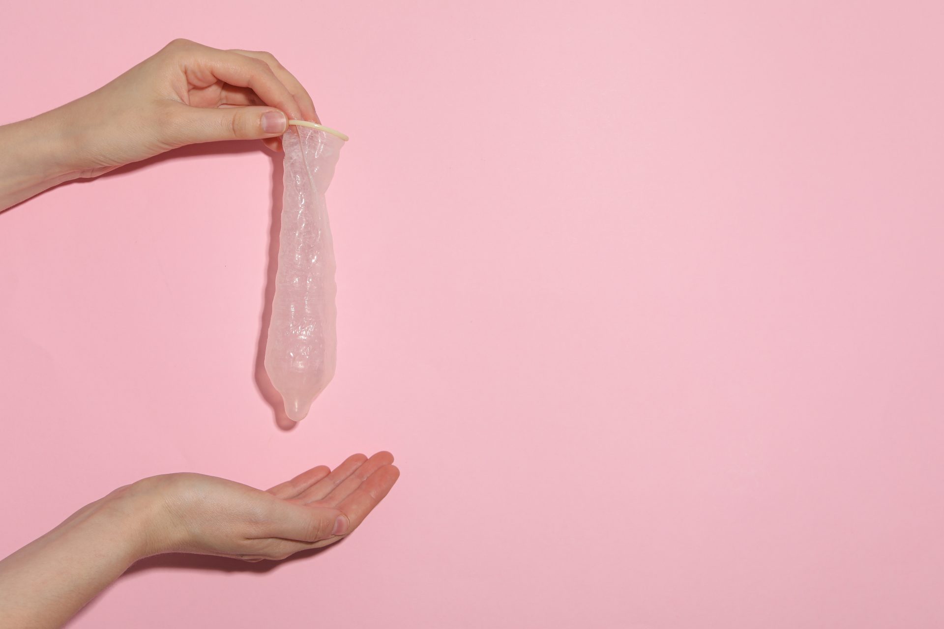 unfolded condom in hand on pink background place 2023 11 27 05 25 22 utc