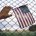 hand holding america flag in front of a barbed fen 2023 11 27 05 06 56 utc
