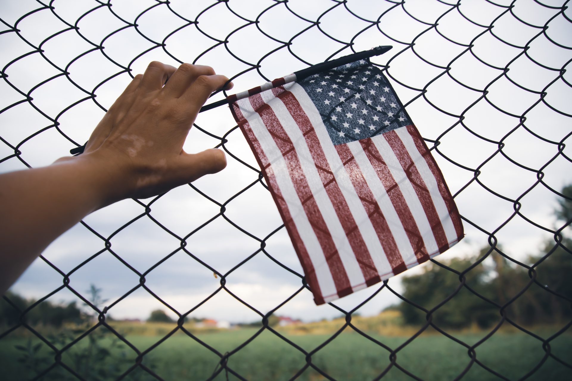hand holding america flag in front of a barbed fen 2023 11 27 05 06 56 utc