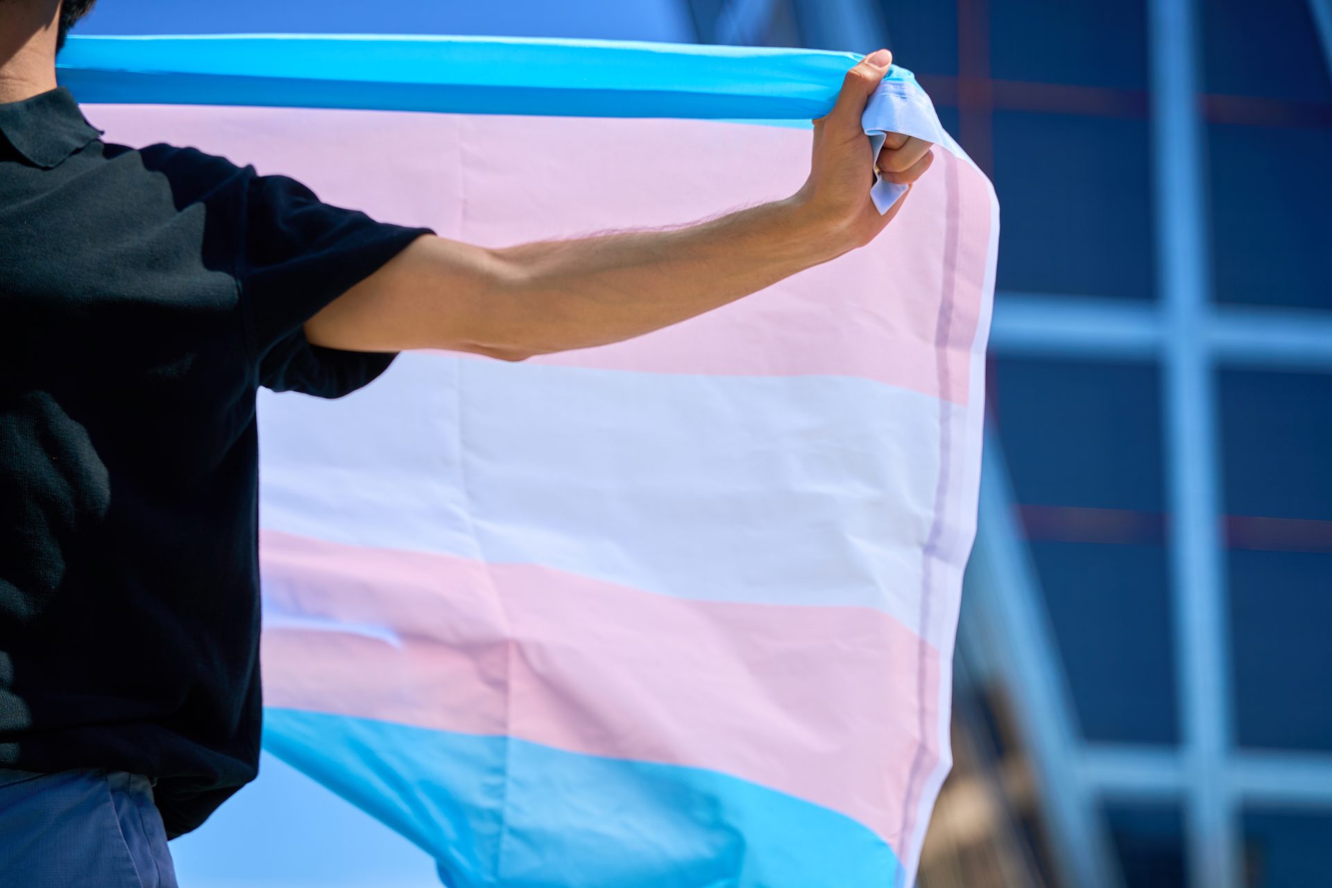 a man holding a transgender flag in front of a bui 2024 12 23 22 26 26 utc