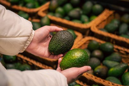 a woman chooses an avocado in a grocery store 2025 03 13 21 26 34 utc