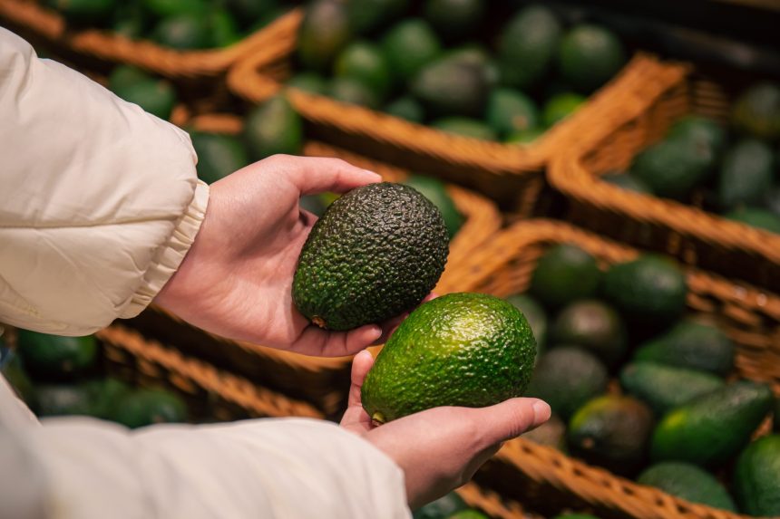 a woman chooses an avocado in a grocery store 2025 03 13 21 26 34 utc
