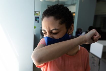 mixed race woman wearing face mask sneezing into h 2026 01 09 11 41 45 utc